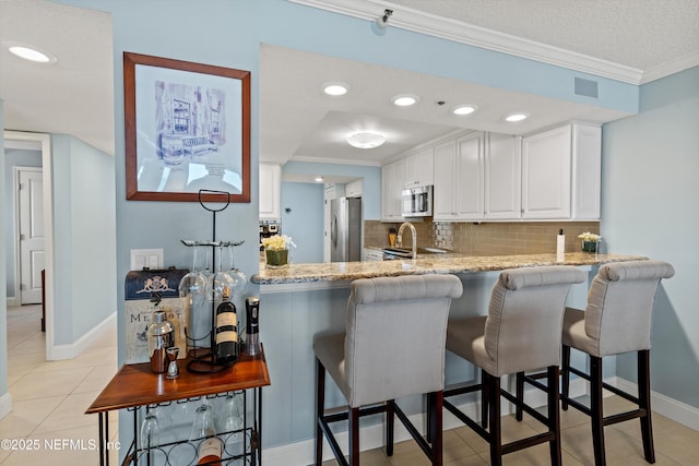 275 1st St S Unit 504, Jacksonville Beach, FL 32250 - kitchen featuring stainless steel appliances, crown molding, white cabinets, decorative backsplash, and light stone counters