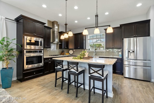 114 Fremont Ave, Saint Augustine, FL 32095 - kitchen featuring a sink, wall chimney range hood, a kitchen breakfast bar, stainless steel appliances, and light wood-style flooring