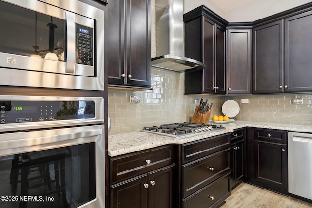 114 Fremont Ave, Saint Augustine, FL 32095 - kitchen with light wood-style flooring, wall chimney range hood, appliances with stainless steel finishes, light stone counters, and decorative backsplash