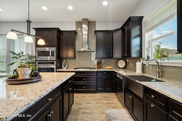 114 Fremont Ave, Saint Augustine, FL 32095 - kitchen featuring light stone countertops, wall chimney range hood, appliances with stainless steel finishes, a sink, and light wood finished floors