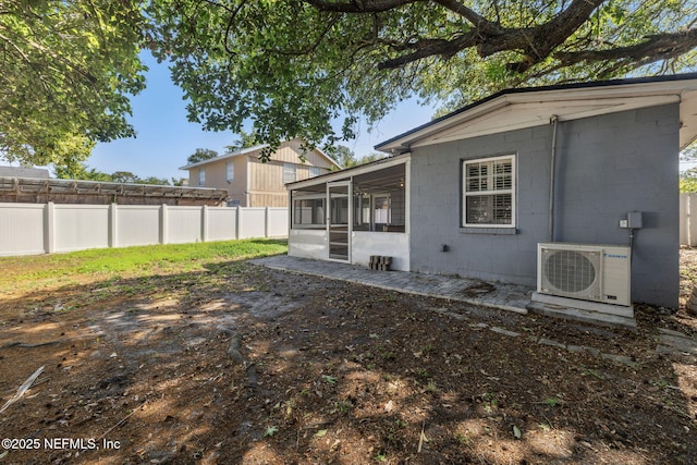 rear view of property with a sunroom, a fenced backyard, concrete block siding, and ac unit