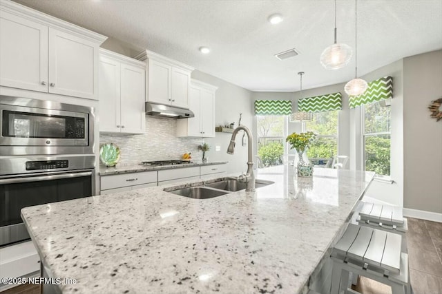 489 Citrus Ridge Dr, Ponte Vedra, FL 32081 - kitchen with a sink, an island with sink, under cabinet range hood, backsplash, and light stone counters