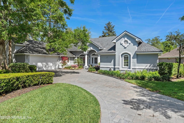 view of front of home with roof with shingles, driveway, an attached garage, a front yard, and stucco siding