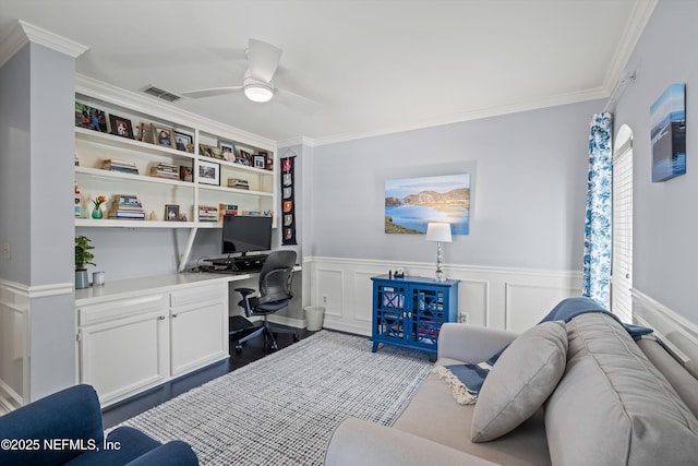 home office with wainscoting, visible vents, a ceiling fan, built in study area, and crown molding