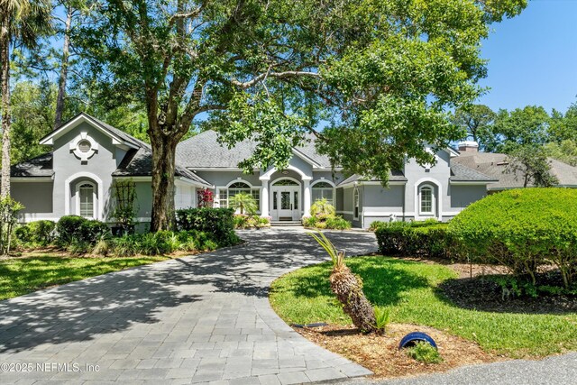 view of front facade featuring a shingled roof, french doors, decorative driveway, and stucco siding