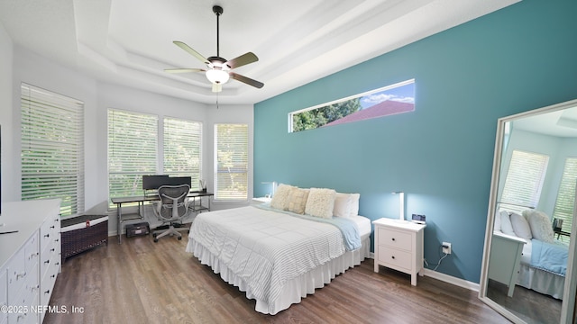 bedroom featuring a raised ceiling, wood finished floors, a ceiling fan, and baseboards