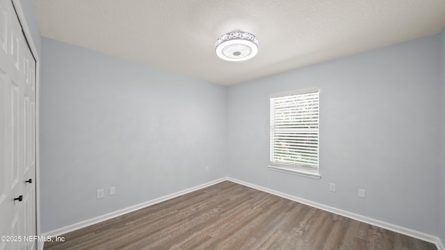 empty room with baseboards, a textured ceiling, and dark wood-type flooring