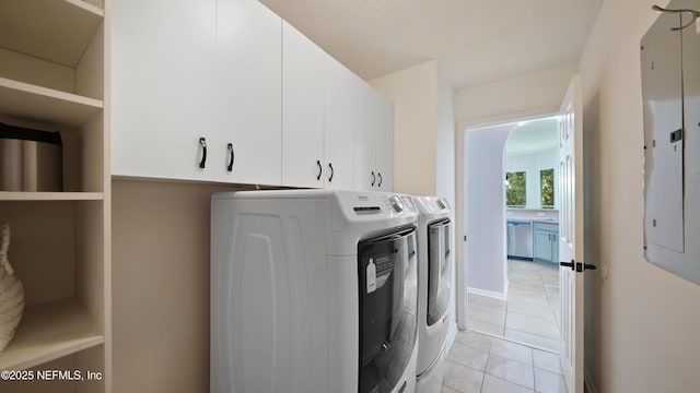 clothes washing area with cabinet space, electric panel, washing machine and clothes dryer, and light tile patterned floors