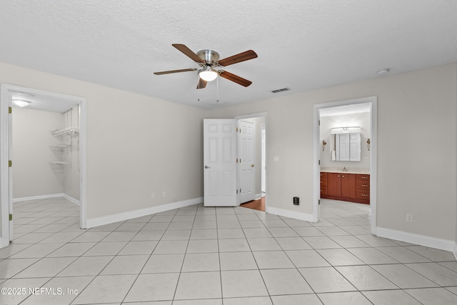 unfurnished bedroom featuring a textured ceiling, a spacious closet, visible vents, light tile patterned flooring, and baseboards