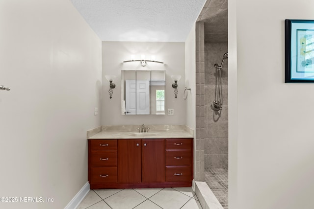 bathroom with vanity, baseboards, tile patterned floors, a textured ceiling, and tiled shower
