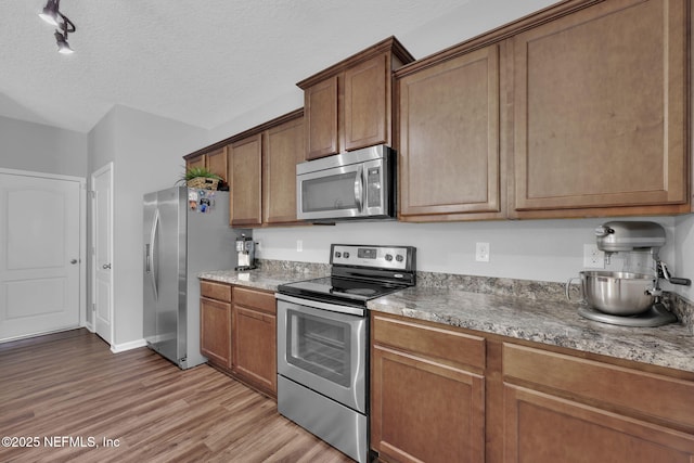 3699 Summit Oaks Dr, Green Cove Springs, FL 32043 - kitchen with light wood-style flooring, a textured ceiling, appliances with stainless steel finishes, and brown cabinetry