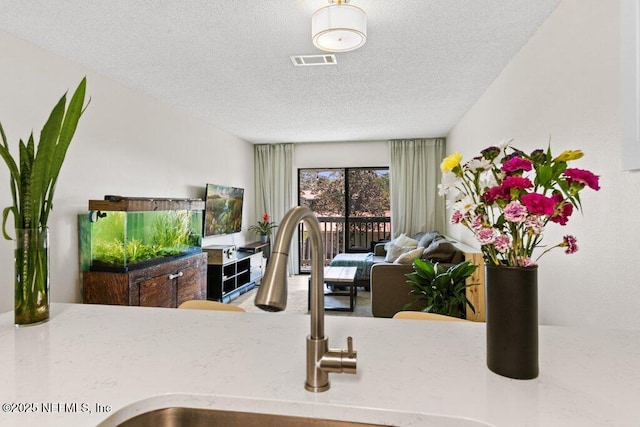kitchen featuring open floor plan, a textured ceiling, a sink, and visible vents
