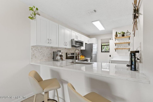 kitchen featuring backsplash, open shelves, visible vents, a breakfast bar area, and appliances with stainless steel finishes