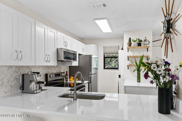 kitchen featuring visible vents, open shelves, a sink, stainless steel appliances, and decorative backsplash