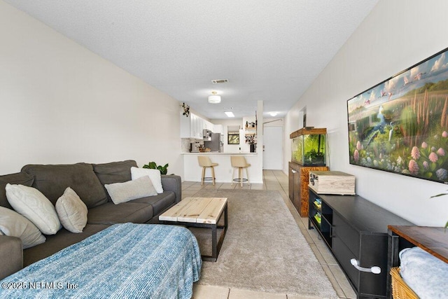 living room with a textured ceiling, light tile patterned flooring, and visible vents