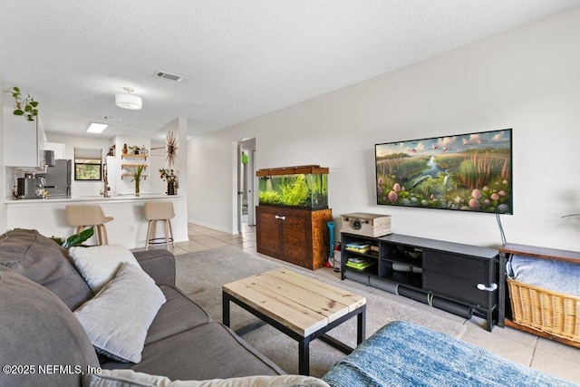 living room featuring visible vents, light tile patterned floors, and a textured ceiling