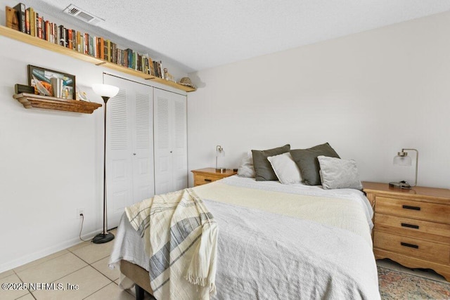 bedroom featuring light tile patterned floors, a closet, visible vents, and a textured ceiling