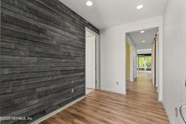 spare room featuring wooden walls, an accent wall, recessed lighting, light wood finished floors, and baseboards