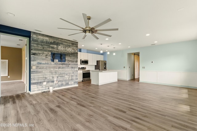 unfurnished living room featuring light wood-style floors, ceiling fan, an accent wall, a barn door, and recessed lighting