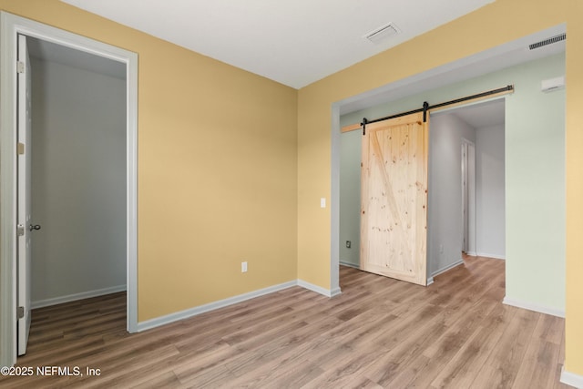 unfurnished bedroom featuring visible vents, baseboards, a barn door, and wood finished floors