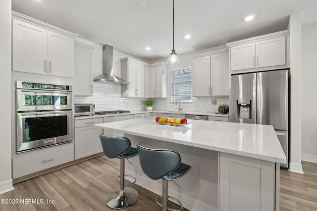 83 Woodgate Dr, Ponte Vedra, FL 32081 - kitchen with a kitchen island, wall chimney exhaust hood, a kitchen bar, stainless steel appliances, and light wood finished floors