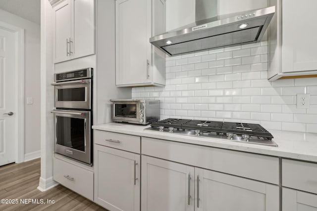83 Woodgate Dr, Ponte Vedra, FL 32081 - kitchen with wall chimney exhaust hood, tasteful backsplash, white cabinets, stainless steel appliances, and light wood finished floors