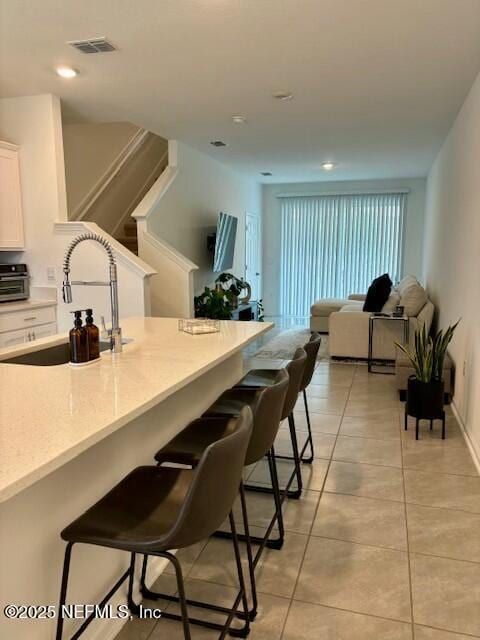 kitchen with visible vents, light tile patterned floors, a sink, a kitchen bar, and white cabinetry
