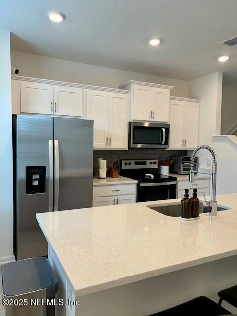 kitchen featuring a sink, white cabinets, appliances with stainless steel finishes, light stone countertops, and visible vents