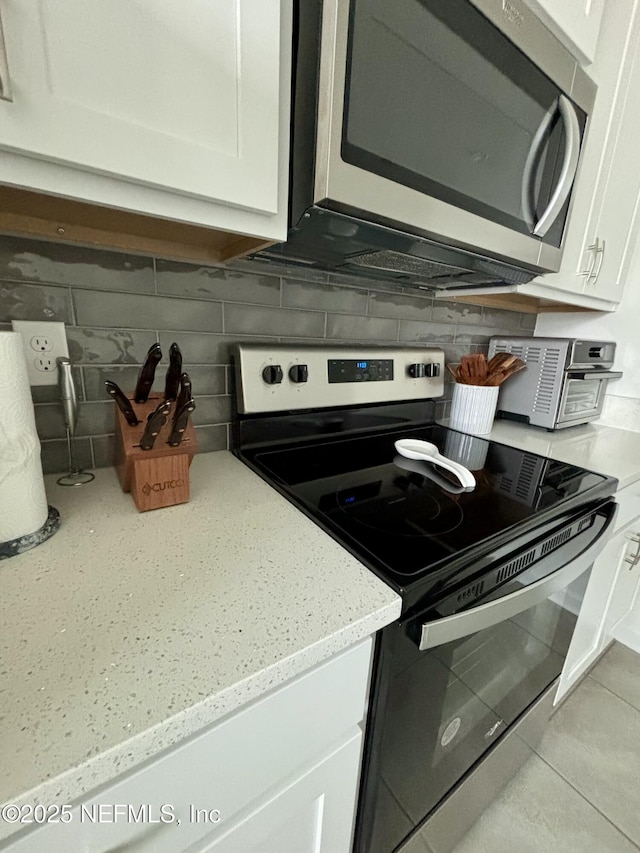 kitchen featuring appliances with stainless steel finishes, tasteful backsplash, light stone counters, and white cabinetry