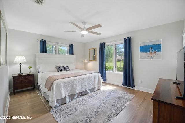 bedroom featuring multiple windows, baseboards, light wood-style flooring, and a ceiling fan
