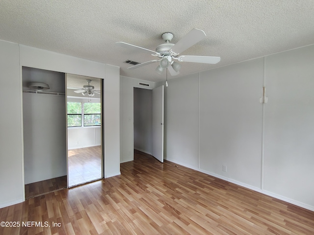 unfurnished bedroom featuring a closet, light wood-type flooring, a textured ceiling, visible vents, and ceiling fan