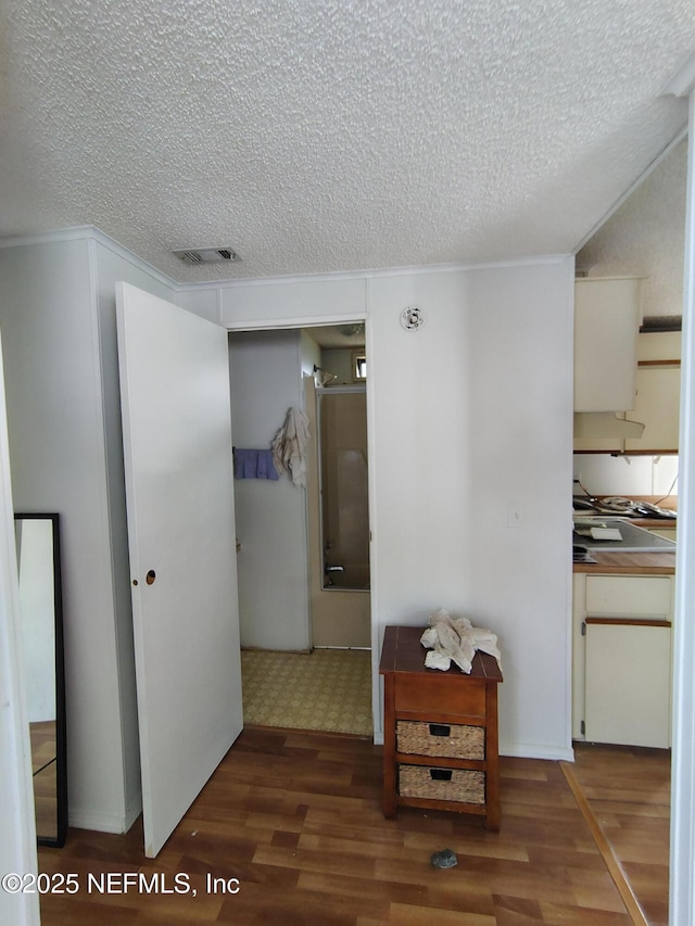 corridor featuring a textured ceiling, wood finished floors, and visible vents