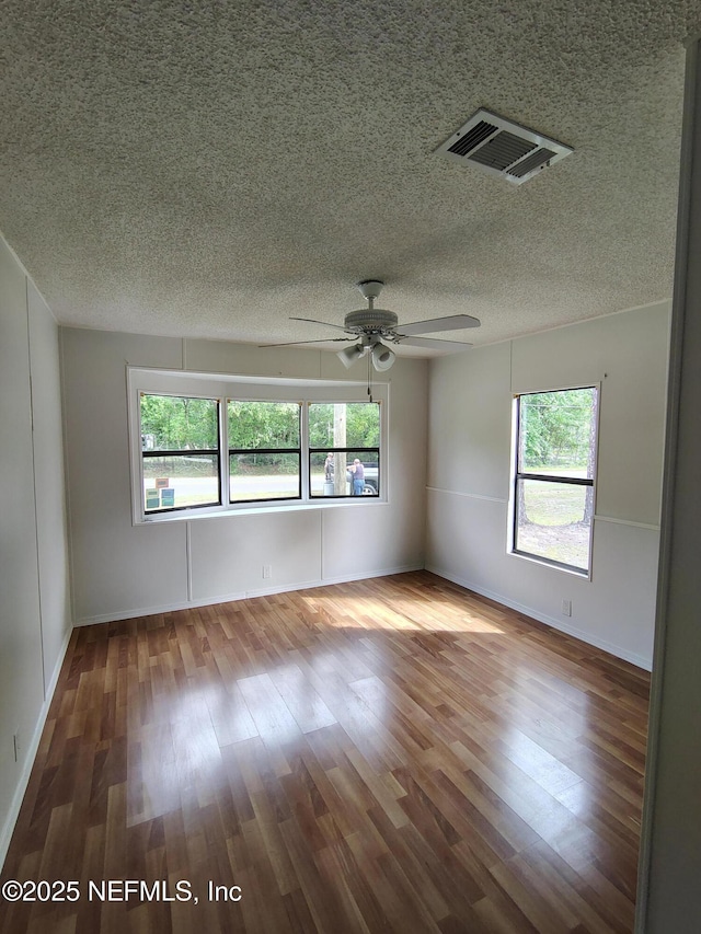 unfurnished room featuring plenty of natural light, visible vents, a ceiling fan, and wood finished floors