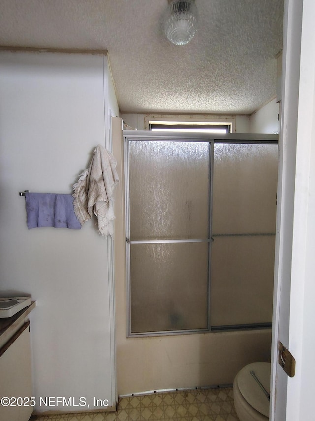 full bath featuring combined bath / shower with glass door, toilet, a textured ceiling, vanity, and tile patterned floors