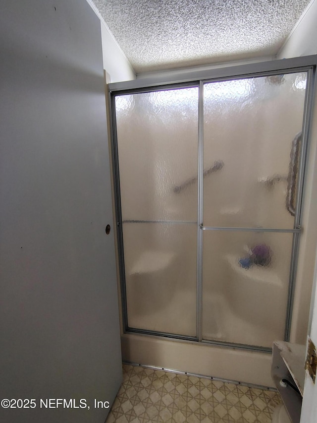 full bath featuring tile patterned floors, a shower with door, and a textured ceiling