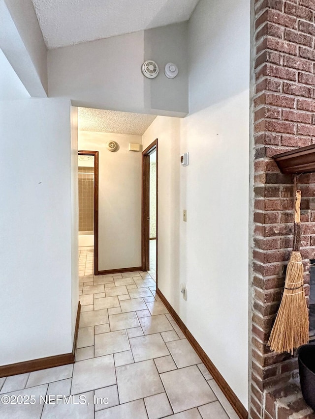 hallway with a textured ceiling, light tile patterned floors, and baseboards