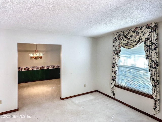 carpeted spare room featuring a textured ceiling and a chandelier