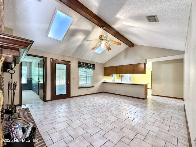 unfurnished living room featuring a ceiling fan, visible vents, vaulted ceiling with skylight, and baseboards