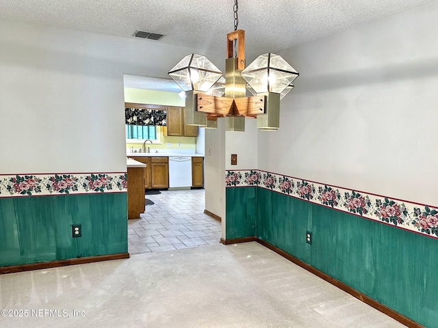 unfurnished dining area featuring a textured ceiling, a sink, visible vents, a wainscoted wall, and light carpet