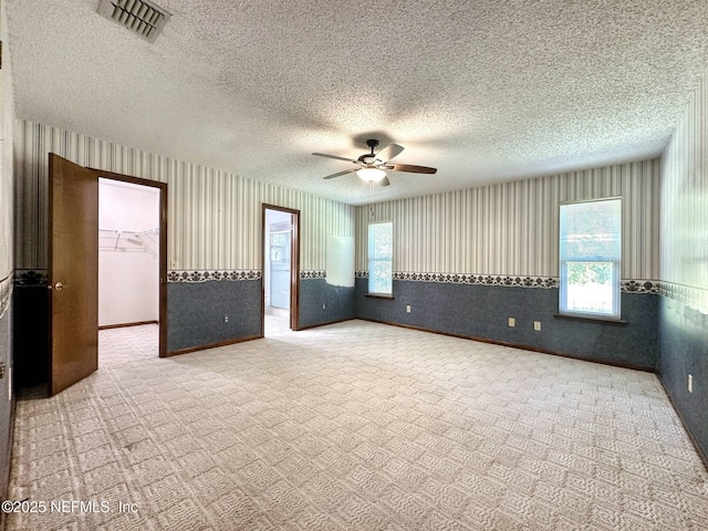 carpeted spare room with visible vents, wallpapered walls, a ceiling fan, and a healthy amount of sunlight