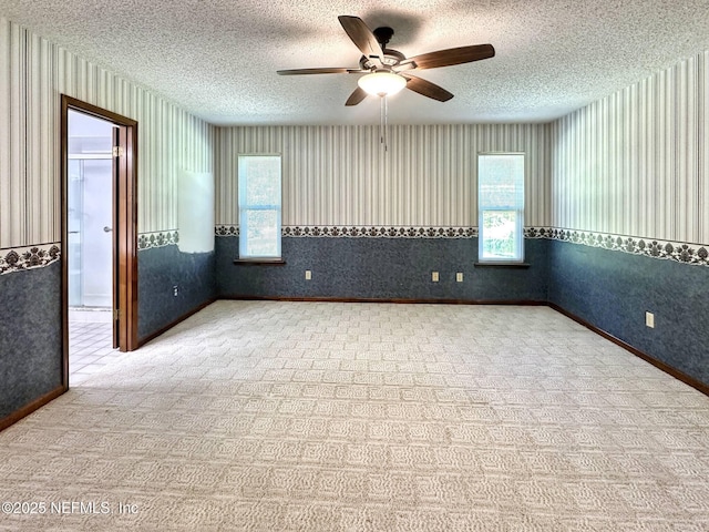 unfurnished room with a textured ceiling, ceiling fan, wallpapered walls, and baseboards