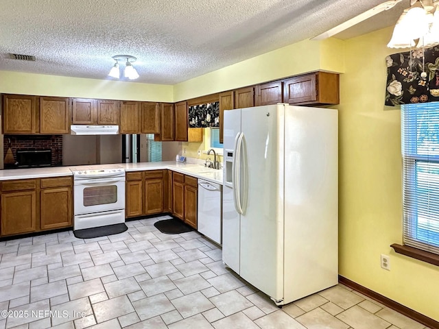 kitchen with white appliances, under cabinet range hood, light countertops, a sink, and visible vents