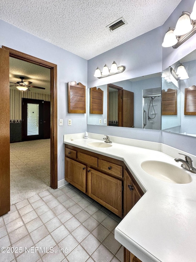 full bath with a textured ceiling, a sink, a shower stall, and visible vents