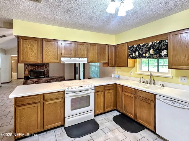 kitchen with white appliances, a peninsula, under cabinet range hood, a sink, and a textured ceiling