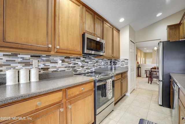 11929 Surfbird Cir Unit 12F, Jacksonville, FL 32256 - kitchen featuring vaulted ceiling, light tile patterned floors, brown cabinets, decorative backsplash, and appliances with stainless steel finishes