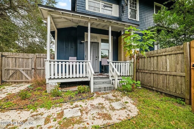 view of exterior entry with a porch and fence