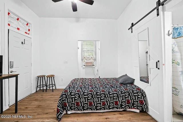 bedroom with wood finished floors, ceiling fan, and a barn door