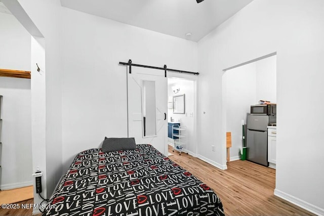 bedroom featuring light wood finished floors, freestanding refrigerator, baseboards, and a barn door