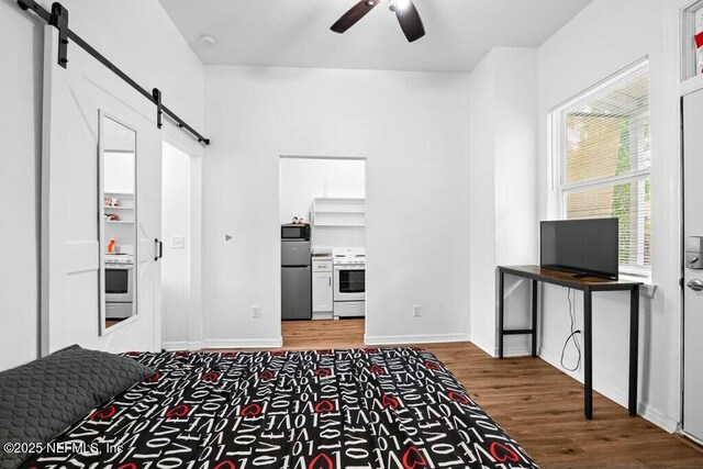 bedroom with ensuite bathroom, baseboards, a barn door, wood finished floors, and stainless steel refrigerator