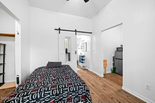 bedroom featuring baseboards, a barn door, freestanding refrigerator, a ceiling fan, and wood finished floors